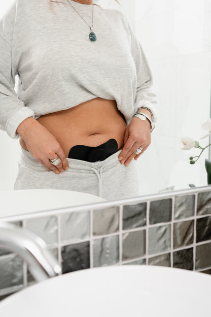 Woman wearing a Tap 2.0 while getting dressed in the bathroom, period relief, pelvic pain relief, easy portable on to go